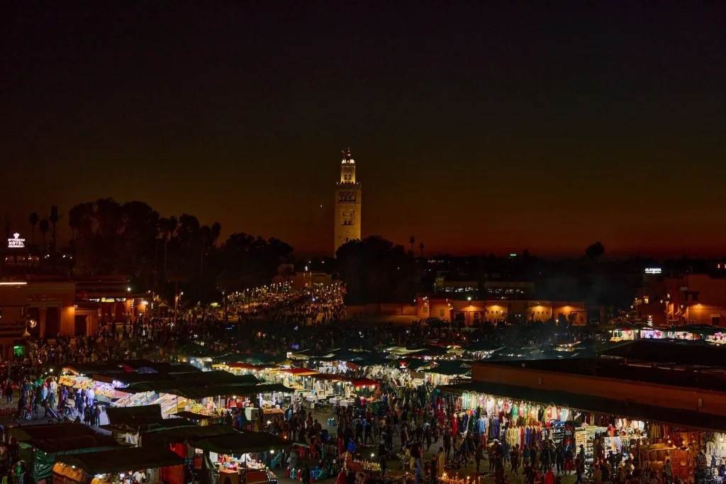 Night market scene with vibrant stalls and the city skyline at dusk.