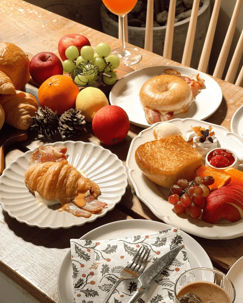 Assorted breakfast items with fruits, pastries, and beverages on a wooden table.