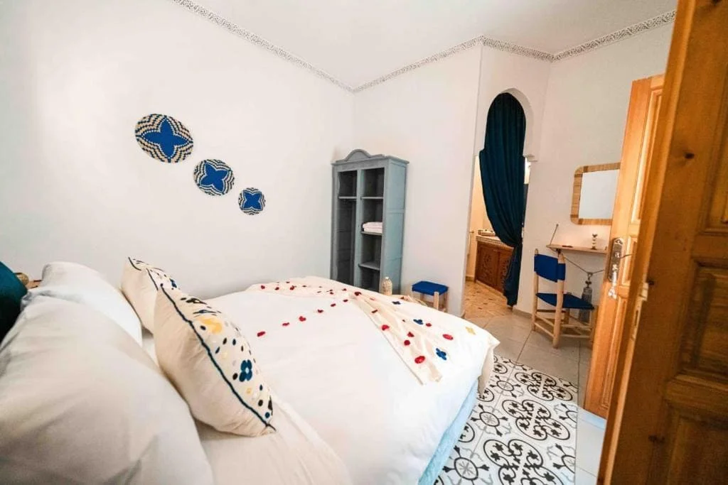 Cozy bedroom with white bedding and blue accents in Riad Kiyanjana Marrakech.