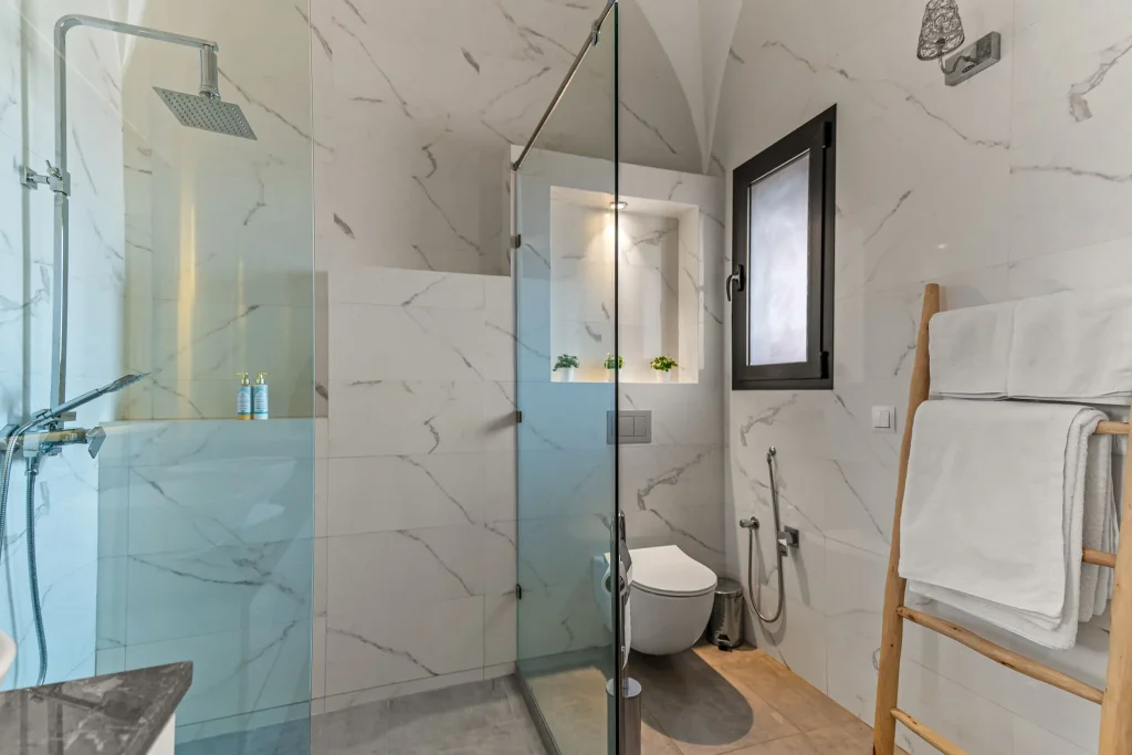 Modern bathroom with marble walls, walk-in shower, and toilet.