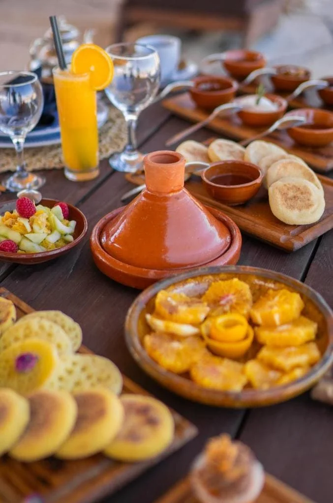 Moroccan food spread with tagine, bread, fruit, and drinks at Riad Kiyanjana Marrakech.