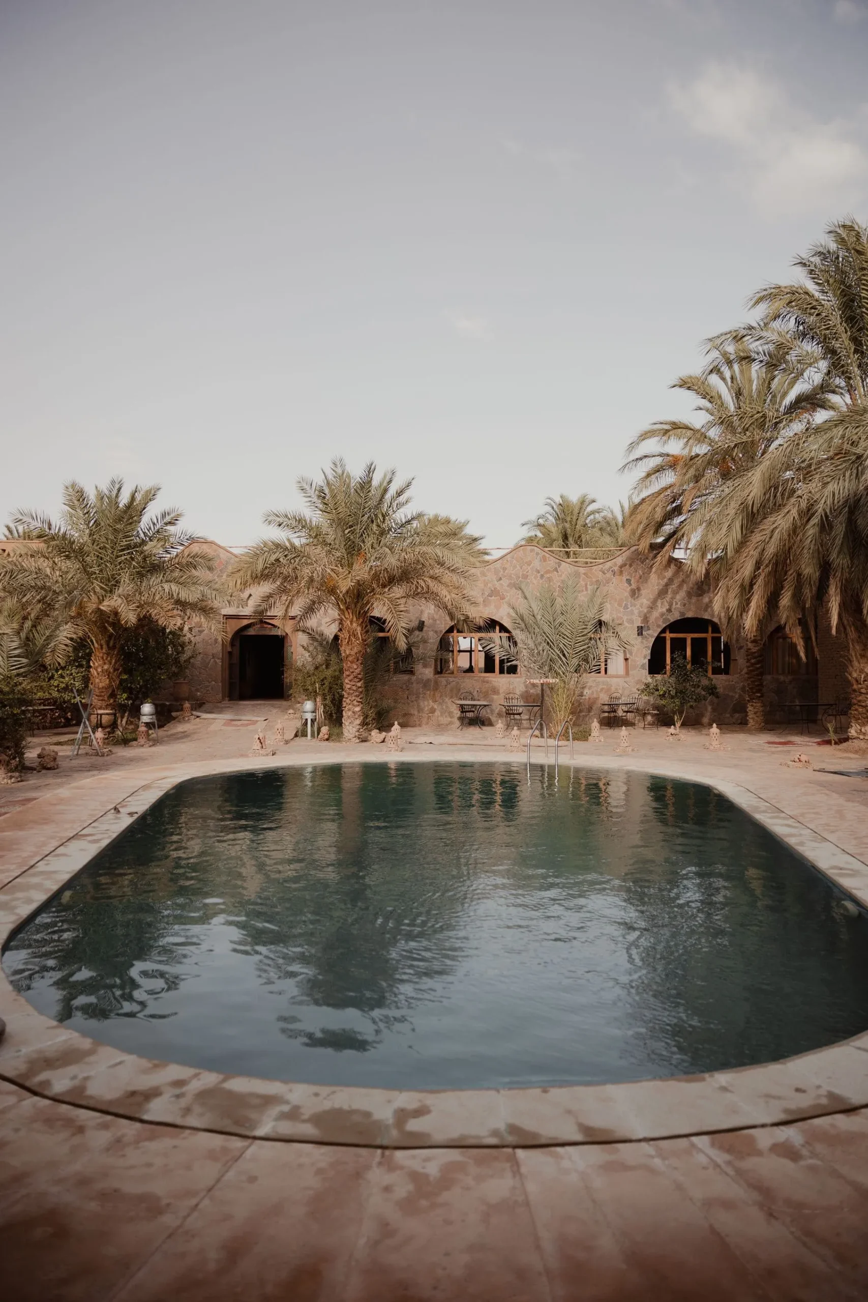 Serene hotel pool surrounded by palm trees and traditional architecture.