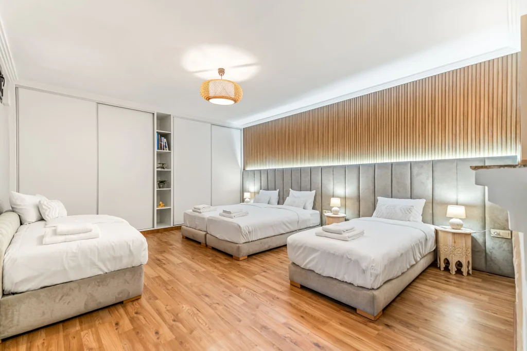 Spacious hotel room with three beds, modern decor, and wooden accents.