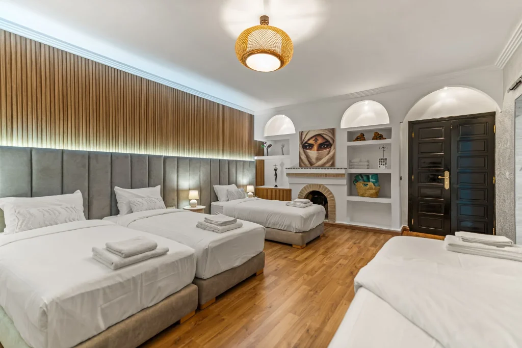 Spacious hotel room with four beds, stylish decor, and elegant lighting.