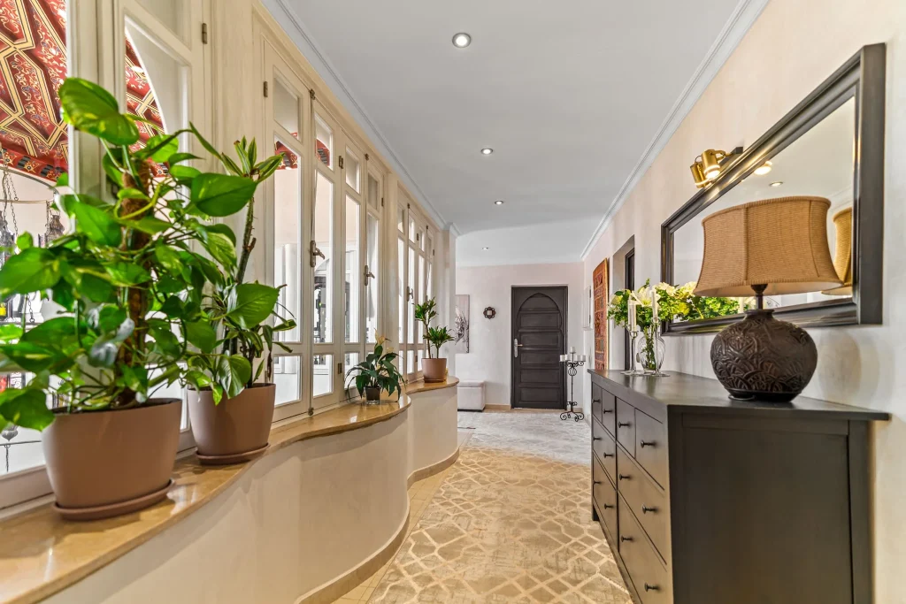 Elegant hotel lobby with plants, mirror, and decorative furniture.
